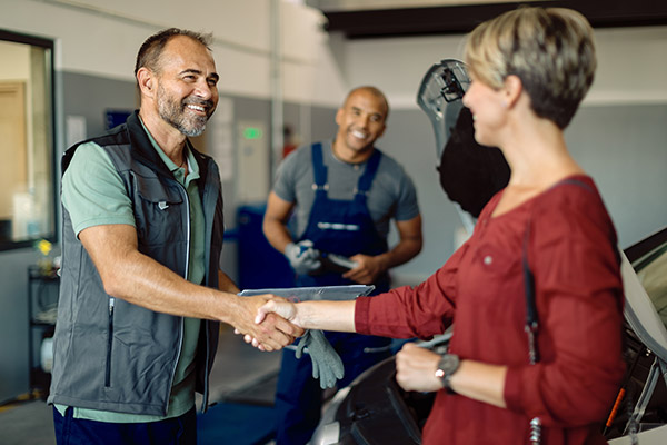 A smiling woman shakes hands with her mechanic after her car has been repaired.