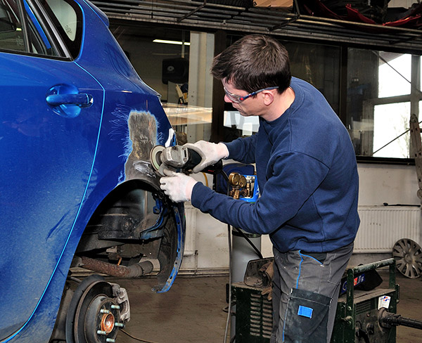 A mechanic works on significant collision damage to a blue car.